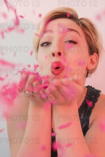 Caucasian woman blowing pink confetti