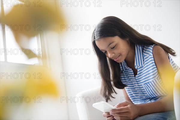 Mixed Race girl sitting in armchair texting on cell phone