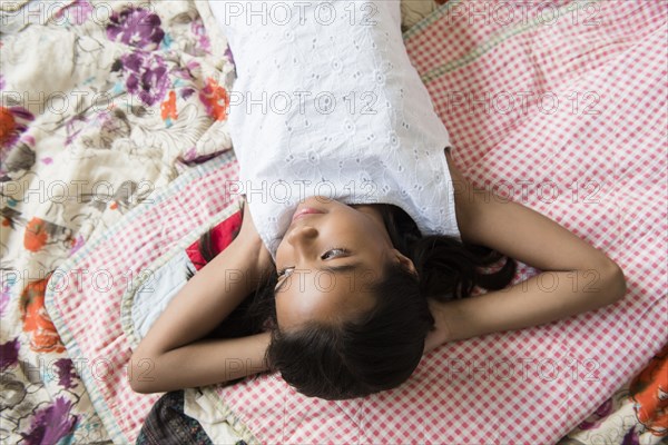 Mixed Race girl laying on bed with hands behind head