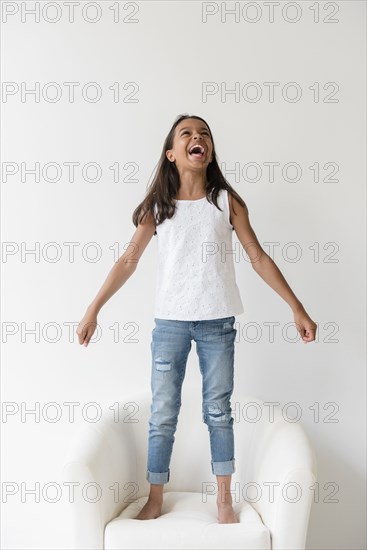 Mixed Race girl standing barefoot on armchair and shouting