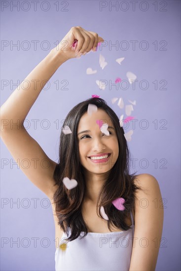 Smiling Mixed Race woman sprinkling heart-shape confetti