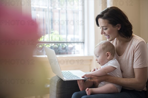 Caucasian mother holding baby in lap using laptop