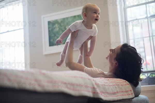 Caucasian mother sitting on sofa lifting baby son