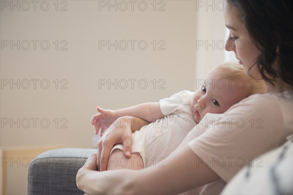 Caucasian mother sitting on sofa cuddling baby son