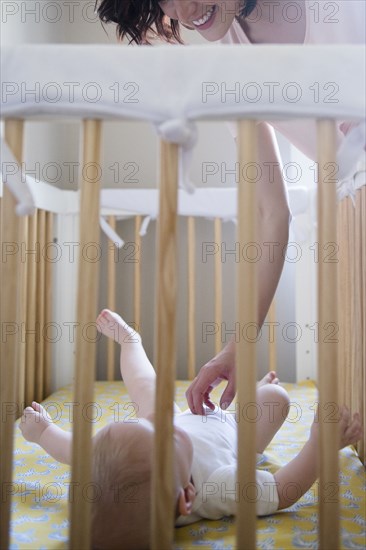 Caucasian mother tickling belly of baby son in crib