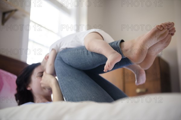 Caucasian mother laying on bed balancing baby son on legs