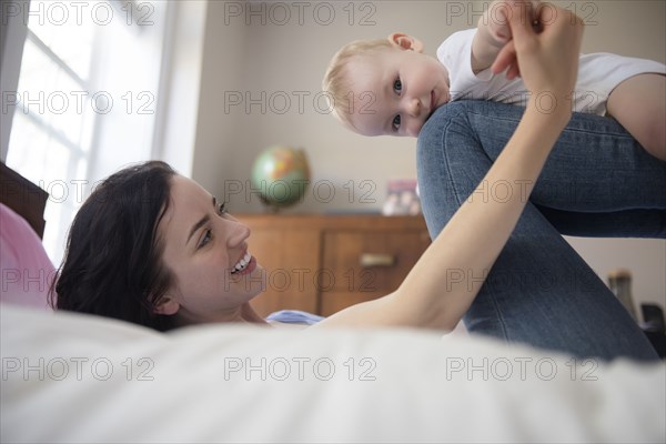 Caucasian mother laying on bed balancing baby son on legs