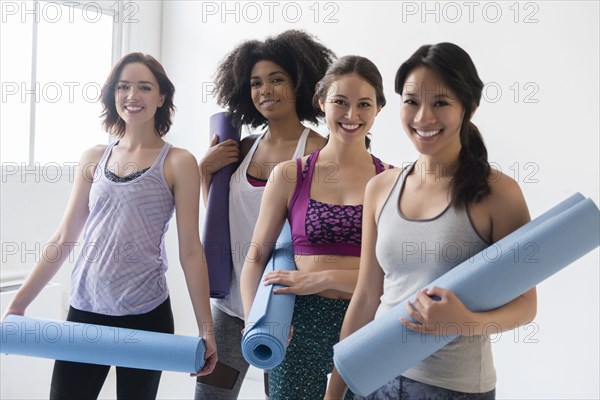 Smiling women holding rolled up exercise mats