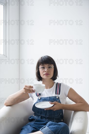 Portrait of Hispanic woman drinking coffee in armchair