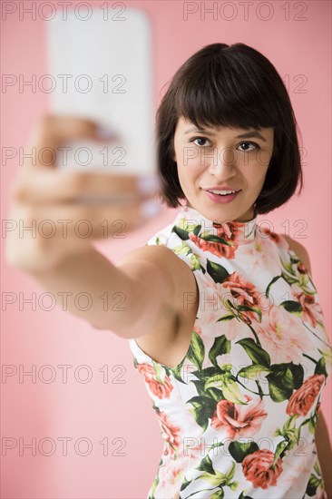 Hispanic woman wearing floral dress posing for cell phone selfie