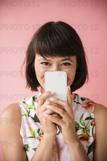 Hispanic woman hiding face behind cell phone
