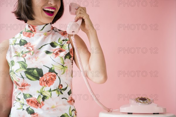 Hispanic woman wearing floral dress holding pink telephone