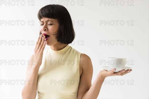Yawning Hispanic woman holding coffee cup