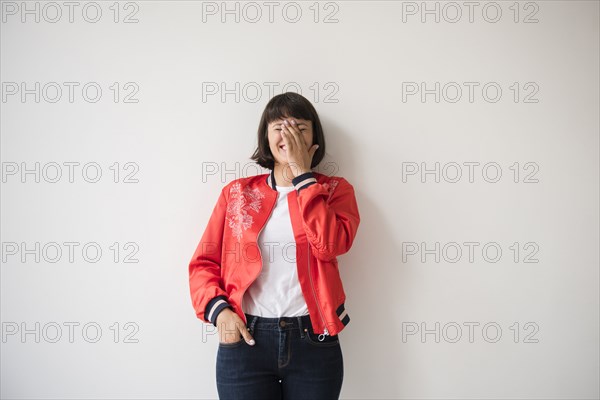 Laughing Hispanic woman wearing red jacket leaning on wall