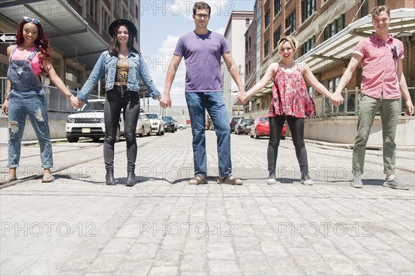 Portrait of smiling friends holding hands in city street