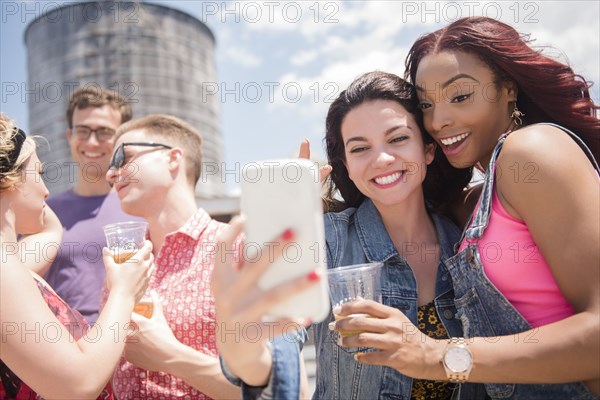 Smiling friends posing for cell phone selfie outdoors
