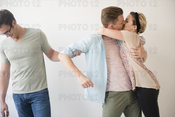 Caucasian man pulling arm of friend kissing girlfriend
