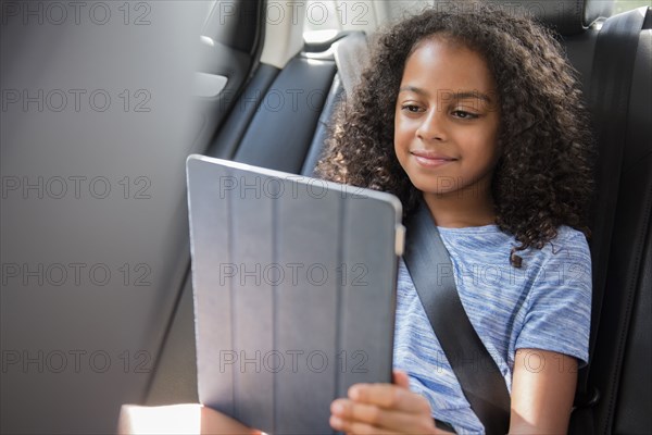 Smiling Hispanic girl using digital tablet in car