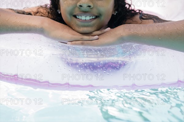 Hispanic girl floating on inflatable ring in swimming pool