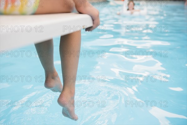 Caucasian girl sitting on diving board over swimming pool