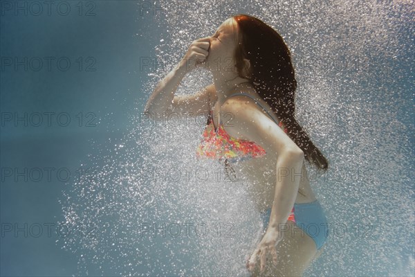 Caucasian girl swimming underwater holding nose