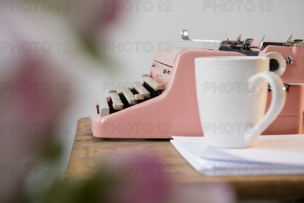 Coffee cup on pile of paper near pink typewriter