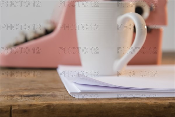 Coffee cup on pile of paper near pink typewriter