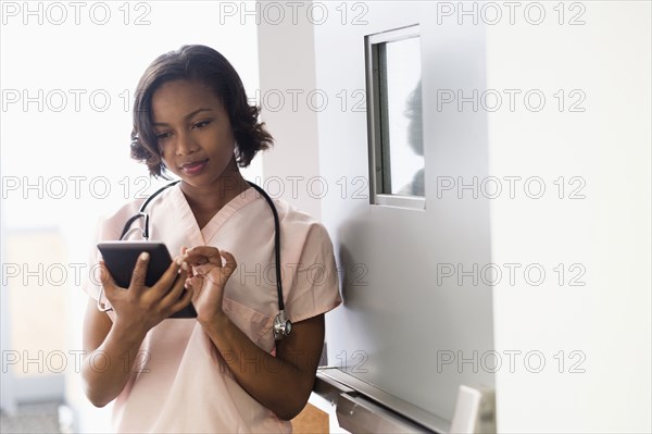 Mixed Race nurse using digital tablet leaning on door