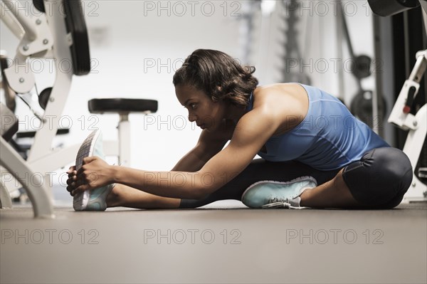 Mixed Race woman stretching legs on floor at gymnasium