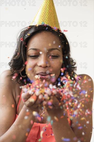 Mixed Race woman wearing party hat blowing confetti