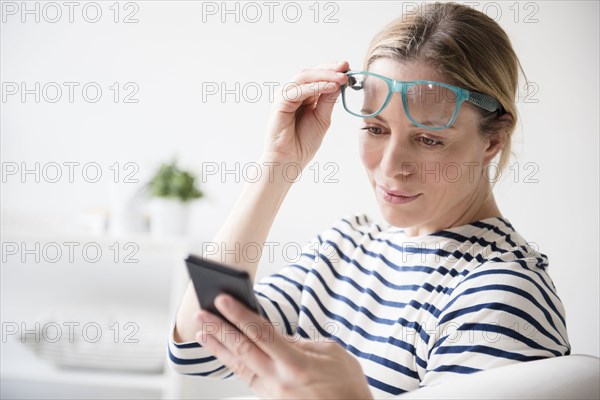 Caucasian woman lifting eyeglasses reading cell phone