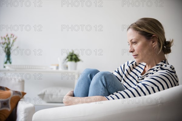 Caucasian woman sitting in armchair holding legs
