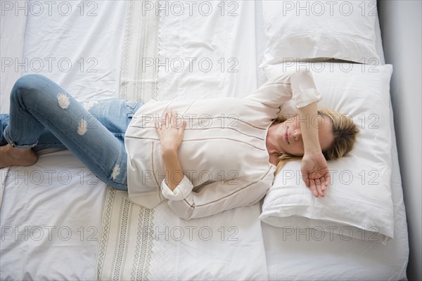 Caucasian woman laying on bed covering eyes