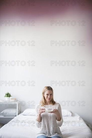 Portrait of Caucasian woman sitting on bed drinking tea