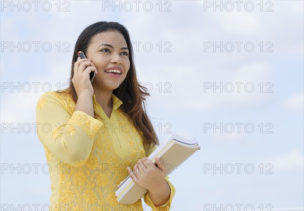 Hispanic woman holding notebooks talking on cell phone