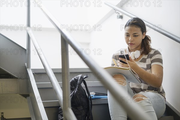 Hispanic woman sitting on staircase texting on cell phone