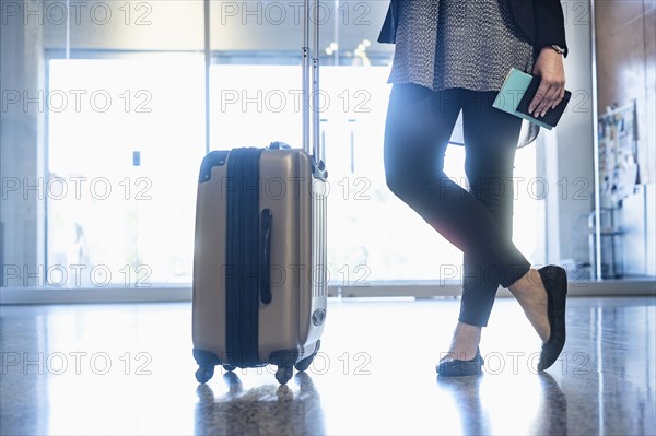 Hispanic woman holding passport standing with suitcase in airport
