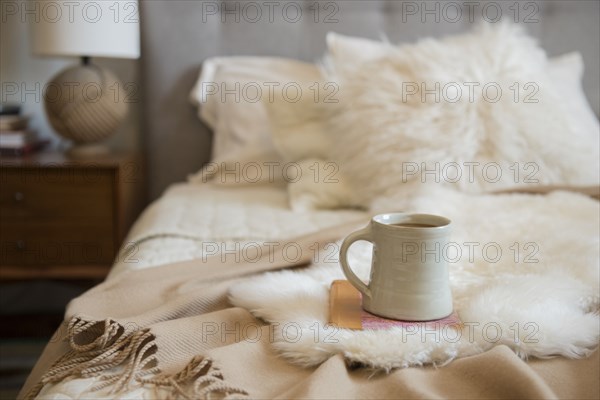 Coffee cup and book on fur on bed
