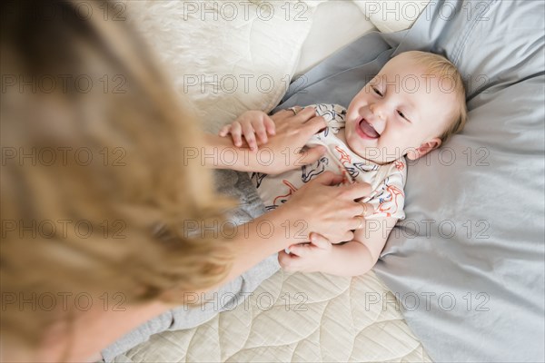 Caucasian mother tickling baby son on bed