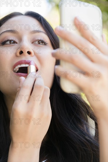 Thai woman holding cell phone applying lipstick