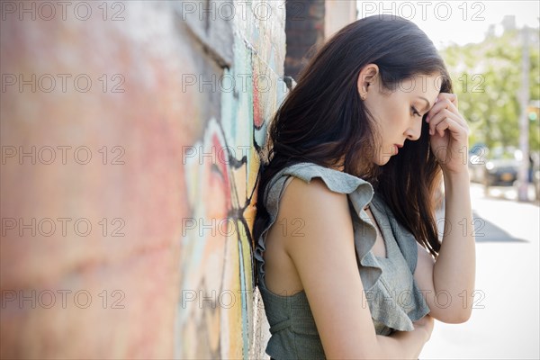 Worried Thai woman leaning on wall in city