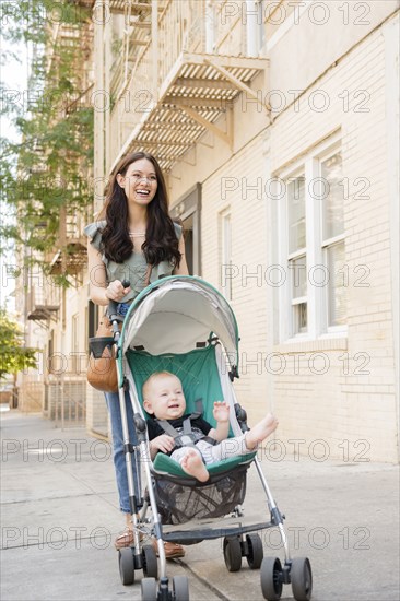 Mother pushing baby son in stroller in city