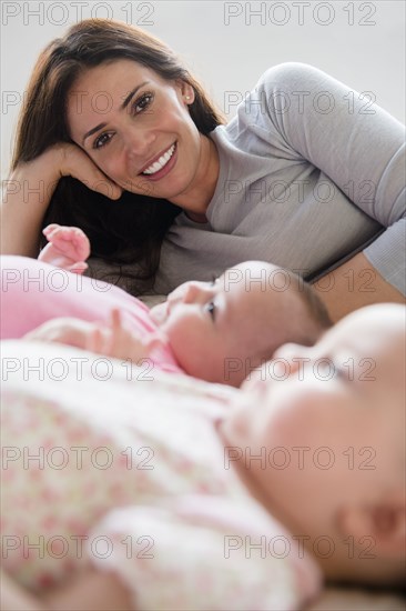 Caucasian mother posing with twin baby daughters on bed