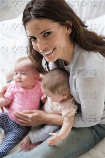 Caucasian mother sitting on bed holding twin baby daughters