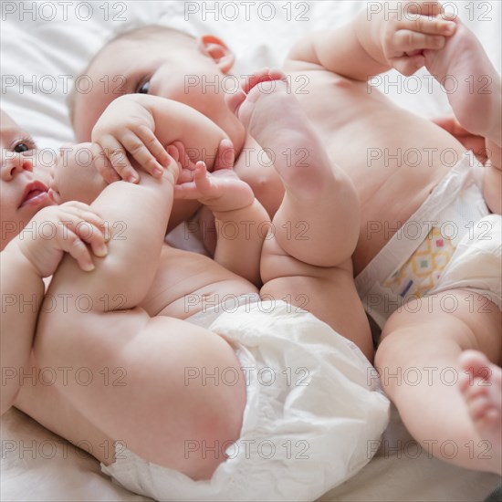 Caucasian twin baby girls wearing diapers on bed