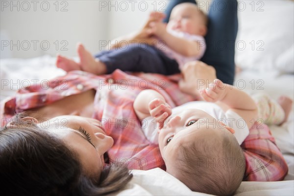 Caucasian mother laying on bed with twin baby daughters