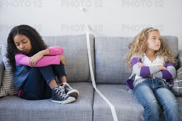 Frustrated girls dividing sofa with tape