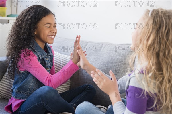 Smiling girls playing clapping game on sofa