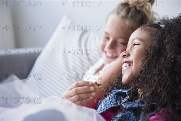 Smiling girls eating cookie on sofa