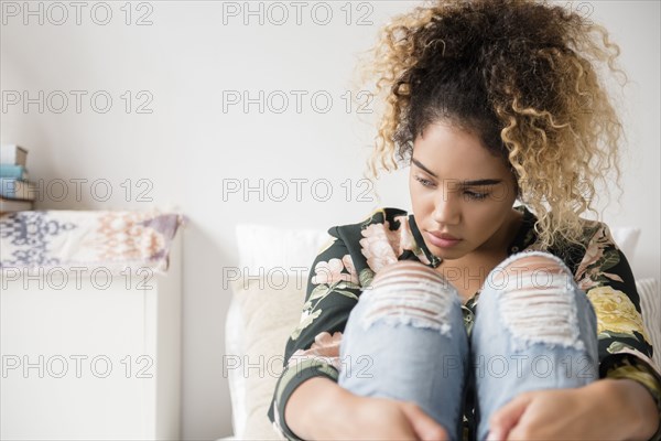 Pensive Mixed Race woman sitting on bed